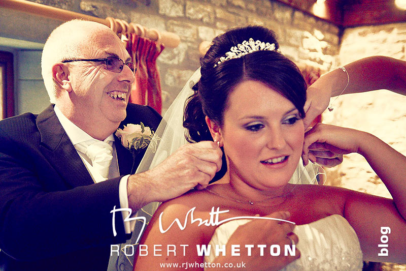 Wedding of Jo and Ben Christie at Kingston Country Courtyard, Swanage Jo's dad putting on her necklace - Dorset Wedding Photographer Robert Whetton