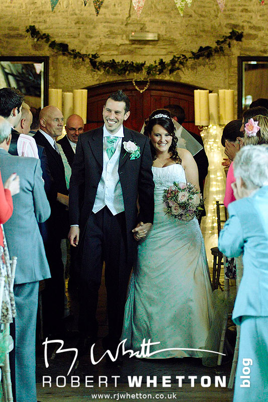 Wedding of Jo and Ben Christie at Kingston Country Courtyard, Swanage Mr and Mrs Christie walk down the isle - Dorset Wedding Photographer Robert Whetton